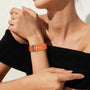 "A fashionable woman wearing a vibrant orange sports watch with a perforated strap, complementing her elegant black off-shoulder outfit."